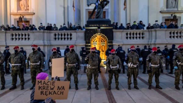 A woman holds a sign reading "You have blood on your hands" near military police and riot police officers standing guards in front of believers praying on the stairs of the Holy Cross Church as protesters take part in demonstration against tightening Poland's already restrictive abortion law, in Warsaw on October 30, 2020. (AFP)