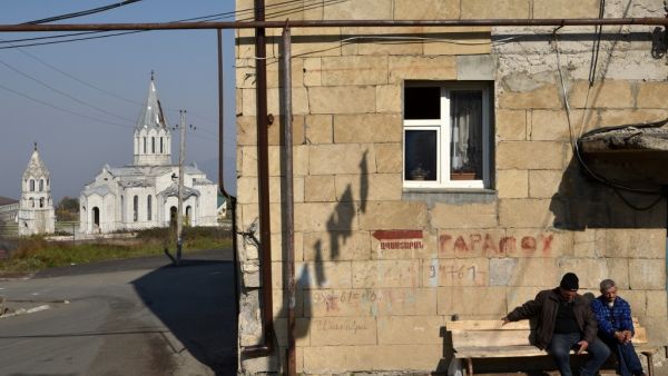 Men sit on a bench in front of residential building not far from the damaged Ghazanchetsots (Holy Saviour) Cathedral in the historic city of Shusha, some 15 kilometers from the disputed Nagorno-Karabakh province's capital Stepanakert, that was hit by a bomb during the fighting between Armenia and Azerbaijan over the breakaway region, on November 1, 2020. Karen MINASYAN / AFP