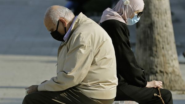 A man and a woman sit back to back on a bench as they enjoy a sunny day near the Beirut seaside promenade on November 24, 2020. JOSEPH EID / AFP