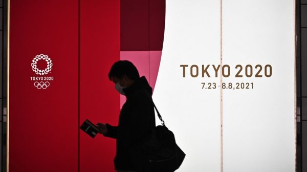A man walks along a corridor past an official Tokyo 2020 Summer Olympics advertisement board in the Shinjuku district of Tokyo on November 30, 2020. Philip FONG / AFP