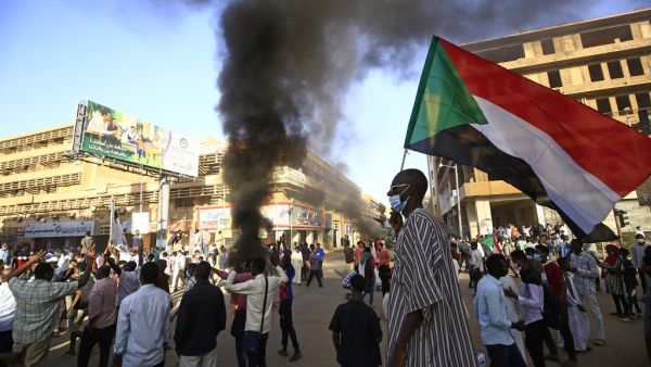A Sudanese man wearing a face mask waves his country's national flag during protests in the capital Khartoum to mark the second anniversary of the start of a revolt that toppled the previous government, on December 19, 2020. Frustrated by the lack of change in their daily lives, thousands of demonstrators, mostly young, marched in several towns in Sudan. ASHRAF SHAZLY / AFP