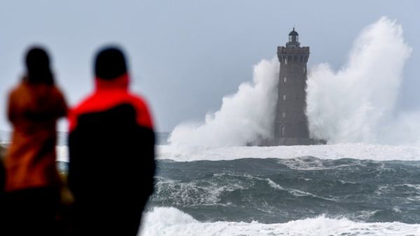 People watch high waves and strong winds hitting The Four Lighthouse (Lighthouse of the Four d'Argenton) at Porspoder, western France on December 27, 2020, as Storm Bella strikes the coast of Britanny. Fred TANNEAU / AFP