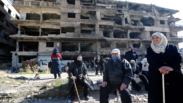 Residents of the Palestinian Yarmuk camp, on the southern outskirts of the Syrian capital Damascus, walk past destroyed buildings on November 25, 2020 as families visit the destroyed residential district.(AFP)
