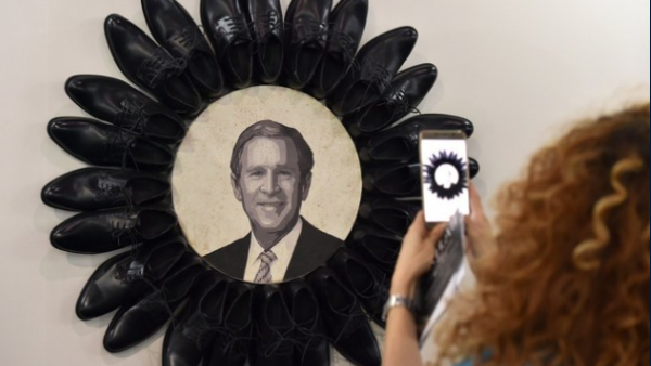 A visitor takes a picture of George W. Bush surrounded by black shoes during the opening of the Beirut Art Fair (Twitter)