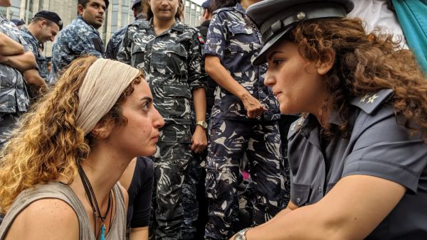 A protester faces off with a police officer during a sit-in on a main road in the Lebanese capital of Beirut, on the tenth day of anti-government demonstrations.  (Shutterstock)	