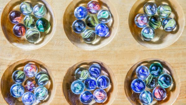 Traditional Mancala boardgame with glass pieces on wooden table  (Shutterstock)	