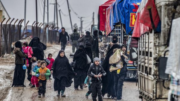 A man carries a child as he walks with other women and children ahead of a member of the Syrian Kurdish internal security services known as Asayish as they head towards trucks, during the release of persons suspected of being related to Islamic State (IS) group fighters from the Kurdish-run al-Hol camp in Hasakeh governorate in northeastern Syria, on January 19, 2021. Delil SOULEIMAN / AFP