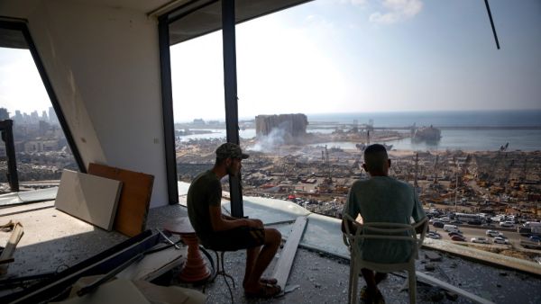 In this file photo taken on August 6, 2020, two men gaze at the devastated Beirut port from a damaged building in the nearby neighbourhood of Mar Mikaehl, two days after a massive blast there shook the Lebanese capital. Six months after a massive explosion ripped through Beirut, donors say that most of the emergency aid they pledged for Lebanon's needy has been disbursed. But some non-governmental organisations say they have hardly received anything, or seen funds they have received lose their value as they