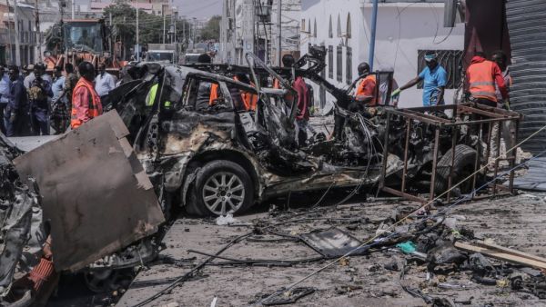 Rescue personnel and bystanders gather near debris at the site of a suicide car bombing attack near a security checkpoint in Mogadishu on February 13, 2021. Three people were killed and eight wounded after a car bomb detonated near a security checkpoint in the Somali capital Mogadishu, a security official and witnesses said. Abdirazak Hussein FARAH / AFP