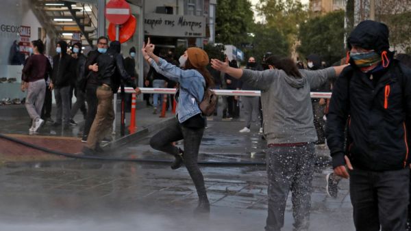 Cypriot protesters react as police fire water cannon to disperse them during a demonstration against government corruption and coronavirus restrictions, in the capital Nicosia on February 13, 2021. Cypriot police used water cannon and tear gas to break up a rare protest in the capital, as hundreds demonstrated against government corruption and coronavirus restrictions. Christina ASSI / AFP