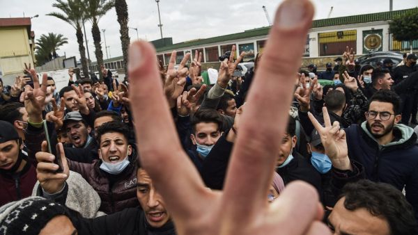 Policemen are seen on the sidelines as students chant slogans while demonstrating in the centre of Algeria's capital Algiers on February 23, 2021 a day after the second anniversary of the "Hirak" protest movement. The "Hirak" protest movement in April 2019 forced longtime president Abdelaziz Bouteflika into resigning. Police were deployed in force in Algiers, with security checkpoints and identity checks carried out around key flashpoints, while helicopters hovering overhead. RYAD KRAMDI / AFP