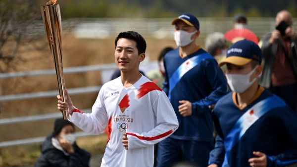 Japanese torchbearer Ryo Matsumoto (L), a student of Nippon Sport Science University, carries an Olympic torch during the first day of Tokyo 2020 Olympic Games torch relay in the town of Naraha, Fukushima Prefecture on March 25, 2021. (Photo: CHARLY TRIBALLEAU / AFP)