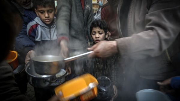 A boy waits as Palestinian Walid al-Hattab (R) distributes soup to people in need during the Muslim fasting month of Ramadan in Gaza City on April 14, 2021, amid the COVID-19 pandemic