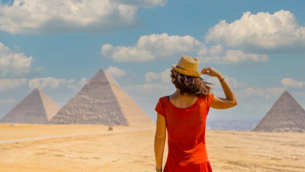 A young tourist in a red dress looking at the Pyramids of Giza