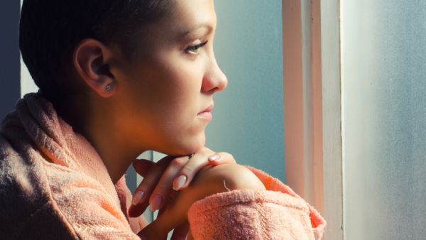 Young depressed cancer patient standing in front of hospital window