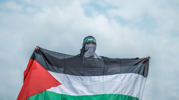 A young teenage Muslim girl wearing abaya and hijab holding a Palestine flag and a head gear with Arabic language means "Brigade AlQassam" which related to an army under Hamas
