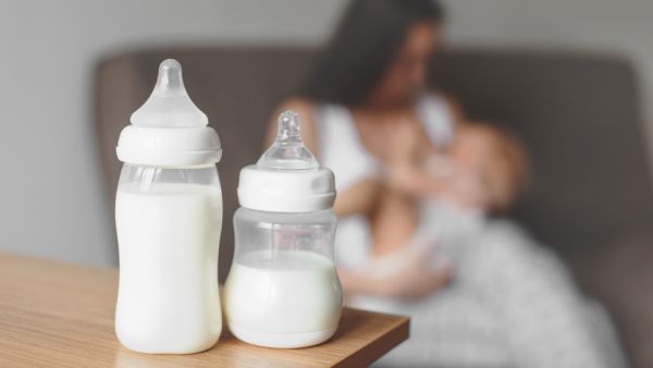 Bottles with breast milk on the background of mother holding in her hands and breastfeeding baby