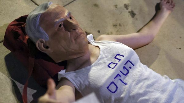 An Israeli protester wears a mask of Prime Minister Benjamin Netanyahu and a T-shirt with a slogan reading in Hebrew: "the ceremony is over", during a demonstration to support the opposition for the formation of a government, on May 31, 2021, in Tel Aviv. Israeli opposition leader Yair Lapid today said many obstacles remain before a diverse coalition can be built to oust veteran Prime Minister Netanyahu, but voiced hope it will achieve the "greater goal"