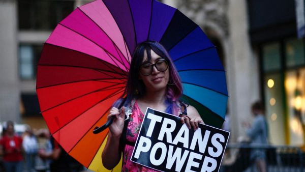 An attendee holds a "Trans Power" sign from under a rainbow umbrella during the annual Dyke March in New York
