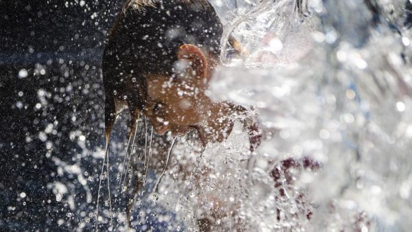 A young boy holds his head under a waterfall at a park in Washington, DC, on June 28, 2021, as a heatwave moves over much of the United States. Swathes of the United States and Canada endured record-setting heat on June 27, 2021, forcing schools and Covid-19 testing centers to close and the postponement of an Olympic athletics qualifying event, with forecasters warning of worse to come. The village of Lytton in British Columbia broke the record for Canada