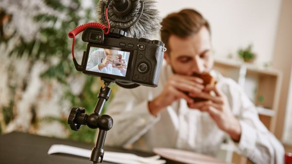 Close up of digital camera screen with male food blogger eating a sandwich while recording video for his vlog.