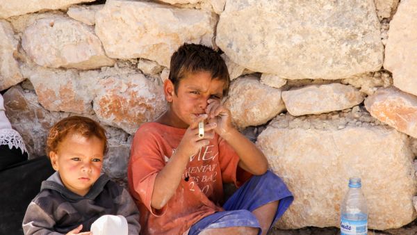 Yong boy playing bamboo flute with his younger brother at the roadside of Roman ruins in Jerash, Jordan