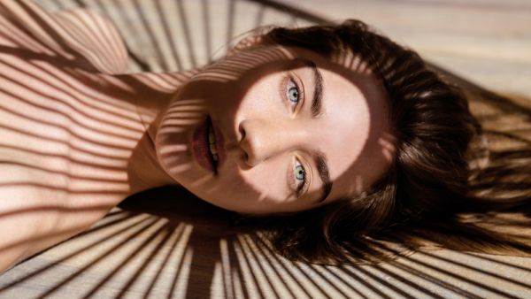 Portrait of beautiful woman with shadows of palm leaf on her face. Concept of sunbathing, vacation.