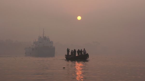 A landscape view of the brahmaputra river national park of the Sundarbans mangrove forest, one of the largest such forests in the world in a foggy day with a small boat full of people