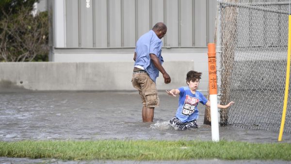 A man and his stepson walk through water in Saint Rose, Louisiana, on August 30, 2021 after Hurricane Ida made landfall. Powerful Hurricane Ida battered the southern US state of Louisiana, leaving at least one dead and knocking out power for more than a million people, including the whole of New Orleans. (Photo by Patrick T. FALLON / AFP) Hurricane Ida death toll rises to five