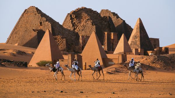 Unidentified Sudanese bedouins ride camels with the famous Meroe pyramids of the ancient Nubian city in the background, on November 02, 2007 in Sudan