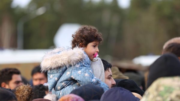 Migrants receive food outside the transport and logistics centre near the Bruzgi border point on the Belarusian-Polish border in the Grodno region on November 22, 2021. (Photo by Andrei POKUMEIKO / BELTA / AFP) migrants want to cross to EU through the Belarus-Poland border