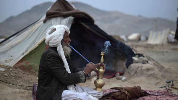 An Afghan internally-displaced man smokes chilam in front of his tent at Shaidayee refugee camp in Injil district of Herat province on February 20, 2022. (Photo by WAKIL KOHSAR / AFP) Western fund freeze on Afghanistan risks humanitarian disaster