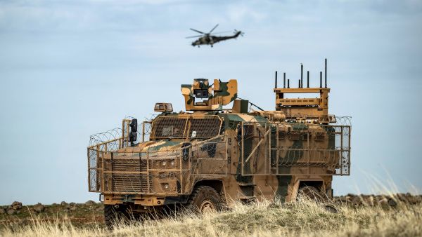 A Russian Mil Mi-24 Hind helicopter gunship flies above a Turkish military vehicle, part of a joint convoy with Russian troops, patrolling in oil fields near the town of al-Qahtaniyah, in Syria's northeastern Hasakeh province close to the Turkish border, on February 4, 2021. / AFP / Delil SOULEIMAN Russian troops