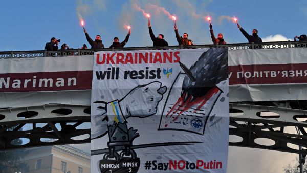 Demonstrators shout slogans as they stand with lit flares on a bridge adorned with a banner 'Ukranians will resist - Say No to Putin' during a rally in Kyiv on February 12, 2022, held to show unity amid US warnings of an imminent Russian invasion. Sergei SUPINSKY / AFP Russian invasion