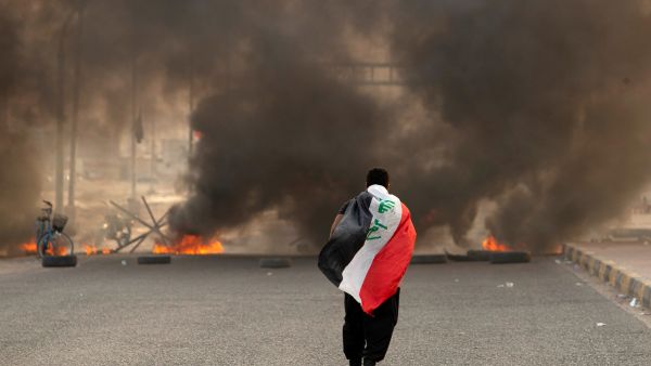 A supporter of Iraqi Shiite cleric Moqtada Sadr carries the Iraqi flag as he walks down a road blocked by burning tyres during a demonstration in Iraq's southern city of Basra on August 29, 2022. (Photo by Hussein Faleh / AFP) Green Zone