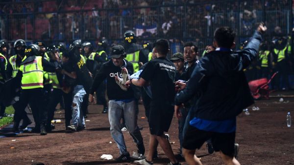 In this picture taken on October 1, 2022, a group of people carry a man after a football match between Arema FC and Persebaya Surabaya at Kanjuruhan stadium in Malang, East Java. At least 127 people died at a football stadium in Indonesia late on October 1 when fans invaded the pitch and police responded with tear gas, triggering a stampede, officials said. (Photo by AFP)