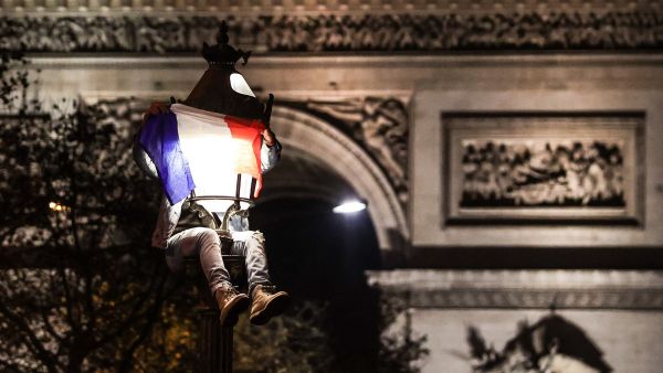 A football fan, sitting on a lamp post next to the Arc de Triomphe, celebrates after France's victory over Morocco in the Qatar 2022 World Cup semi-final, on the Champs-Elysees in Paris on December 14, 2022. (Photo by Thibaud MORITZ / AFP)