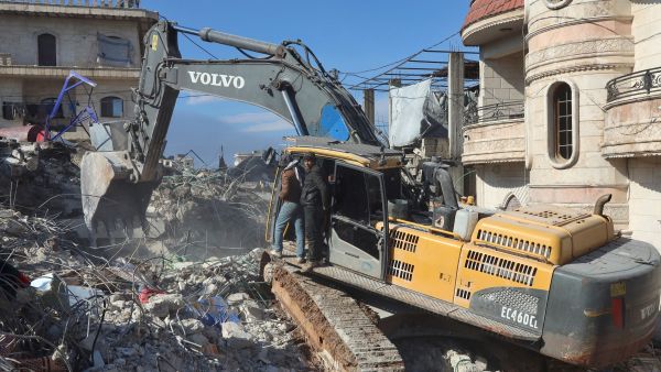 Syrian rescuers use an excavator to shift through the rubble 