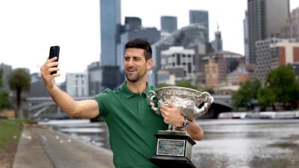 This handout picture released by Tennis Australia on January 30, 2023, shows Serbia's Novak Djokovic takes a selfie with the Norman Brooks Challenge Cup next to the boat sheds on the Yarra River, the same spot of his first Australian Open trophy celebrations, in Melbourne. (Photo by FIONA HAMILTON / TENNIS AUSTRALIA / AFP)