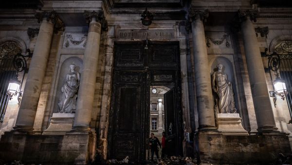 People stand next to the gate of the city hall after it was set on fire by protesters after a demonstration, a week after the government pushed a pensions reform through parliament without a vote. (Photo by PHILIPPE LOPEZ / AFP) pension reform