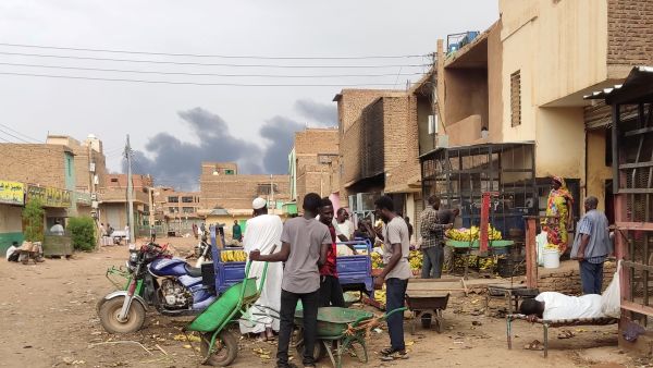 Smoke rises above buildings as people gather at a market to buy food provisions, in Khartoum. (Photo by AFP) Khartoum