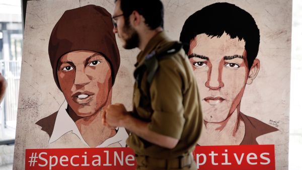 جندي اسرائيلي يمر من امام لوحة رسم عليها صورتا هشام السيد وأفراهام منغيستو المحتجزين لدى حماس