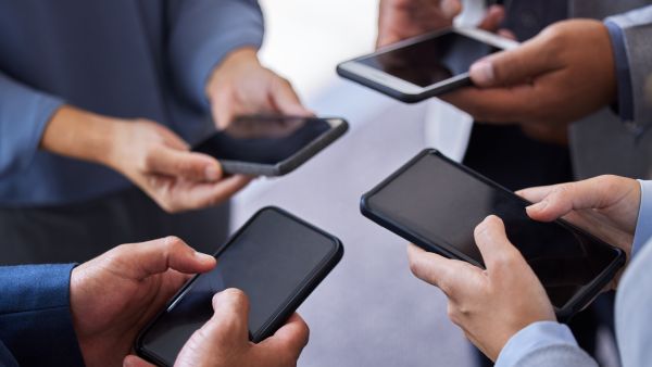 businesspeople standing together in the office and using their cellphones.