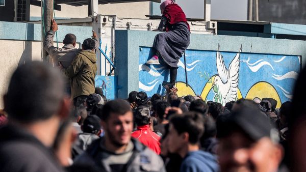 سيدة تتسلق جدران أحد مستودعات "الأونروا"  بعد انتظارها في طابور الحصول على حصص الطحين، في رفح جنوب غزة