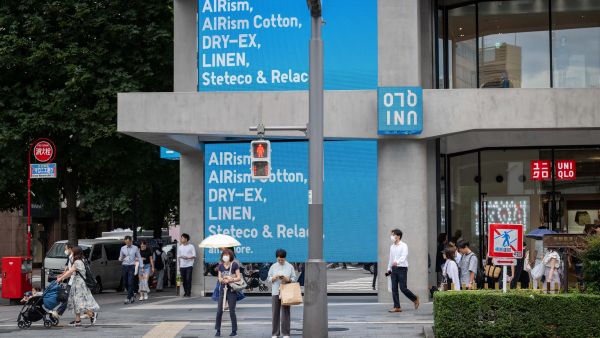 People wait to cross a street outside a branch of the Fast Retailing clothing brand Uniqlo along a street in Tokyo on July 11, 2024. (Photo by Yuichi YAMAZAKI / AFP) Japan