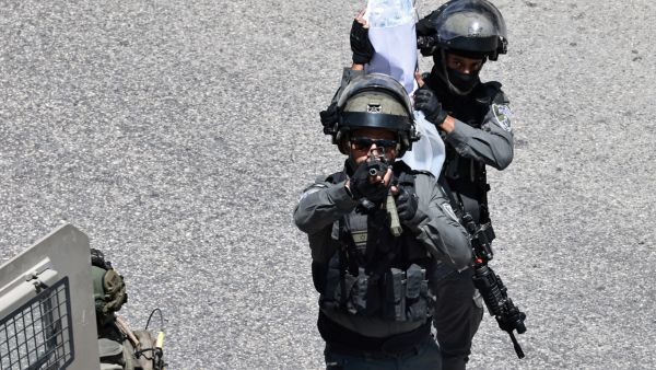 An Israeli army soldier points his rifle as another carries plastic bags during a raid on a currency exchange shop in Ramallah, in the occupied West Bank on May 27, 2025. (Photo by Zain JAAFAR / AFP) Israeli army
