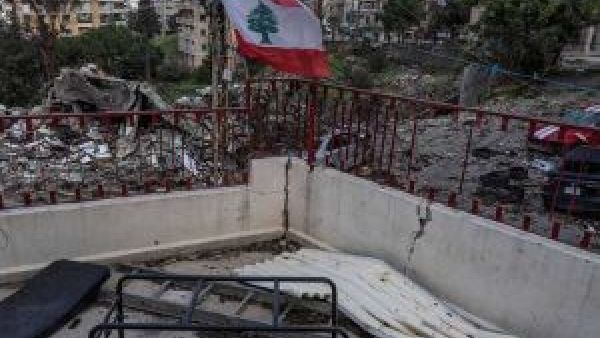 علم لبنان يرفرف فوق منطقة متضررة بفعل العمليات العسكرية في جنوب لبنان، مع ظهور آثار الدمار في محيط المباني السكنية.