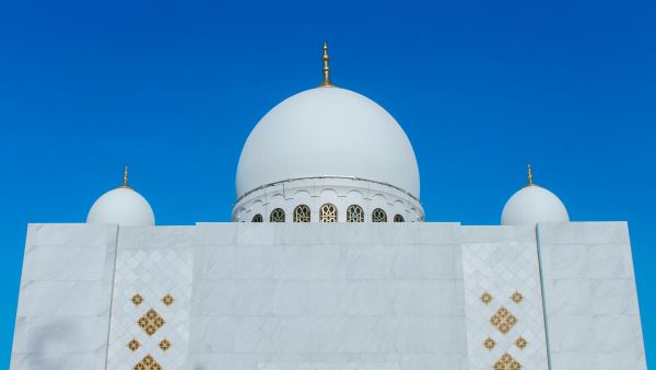 واجهة مسجد بقباب بيضاء بارزة تحت سماء زرقاء صافية، في صورة تعبيرية عن دور العبادة الإسلامية.