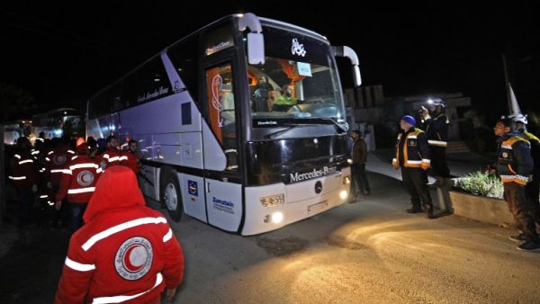 Members of the Syrian Red Crescent and Civil Defence stand by as a convoy of buses carrying rebel fighters and civilians from the Eastern Ghouta enclave town of Harasta arrives in the town of Qalaat al-Madiq, about 45 kilometres northwest of the central city of Hama, early on Mar. 23, 2018. 
(OMAR HAJ KADOUR / AFP)