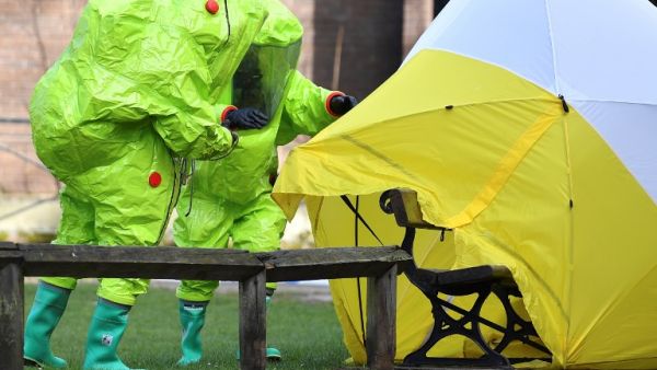 (FILES) In this file photo taken on Mar. 8, 2018 members of the emergency services in green biohazard encapsulated suits afix the tent over the bench where where former Russian spy Sergei Skripal and his daughter Yulia were found on Mar. 4 in critical condition at The Maltings shopping centre in Salisbury, southern England, after the tent became detached. (Ben STANSALL / AFP)